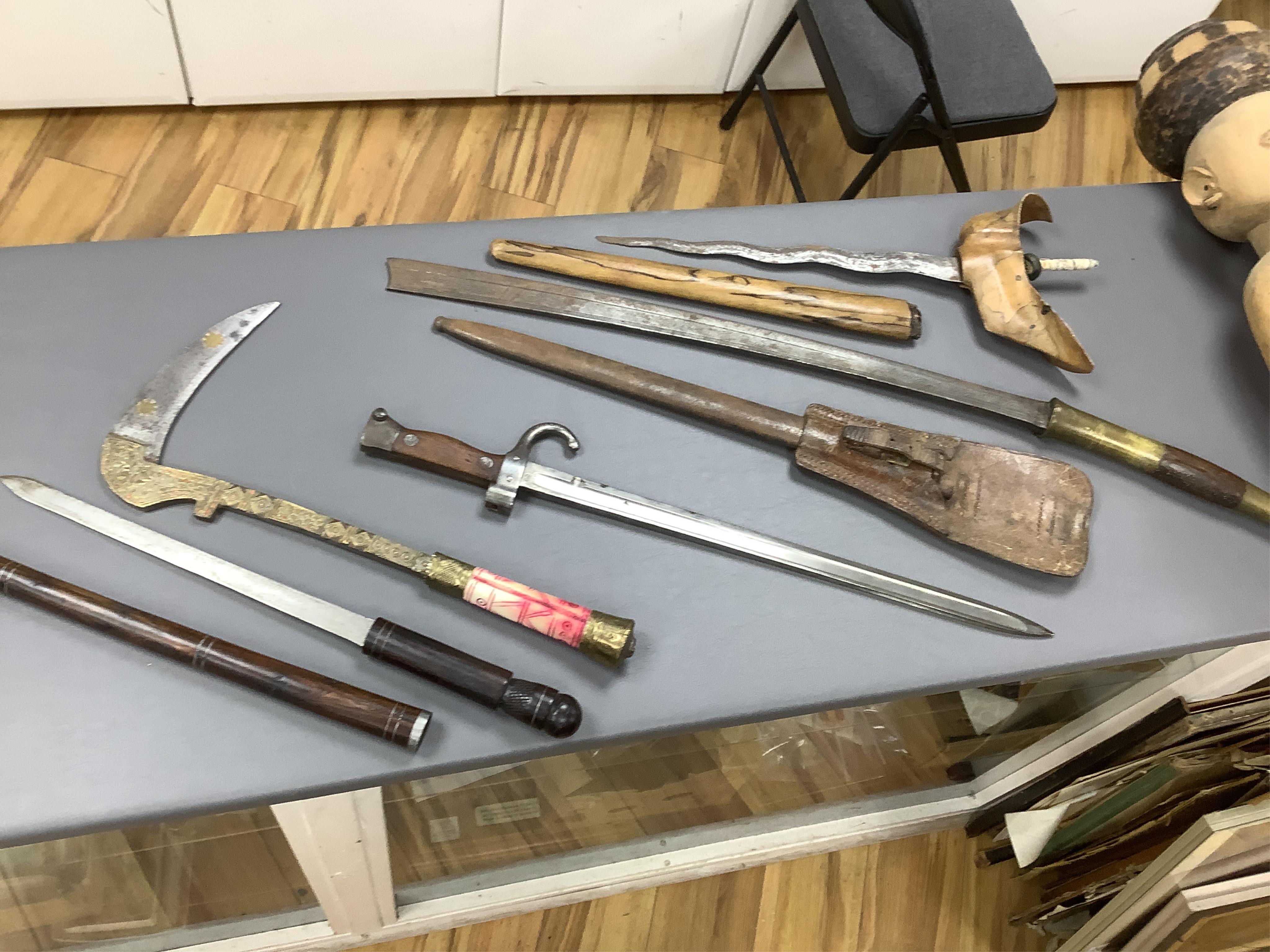 Eighteen assorted world weapons comprising a silver jambya (pommel missing), a knobkerry, a dha, two kris (one with handle missing), a lohar, three kukris, a djambok, a Chinese trousse, a chora, a flyssa, five others and